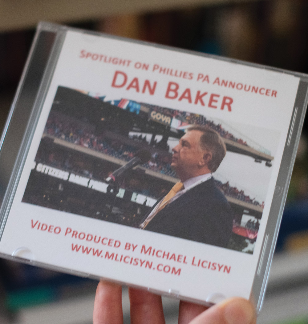 a CD disc case with a cover that reads "Spotlight on Phillies PA Announcer Dan Baker" is held in a hand