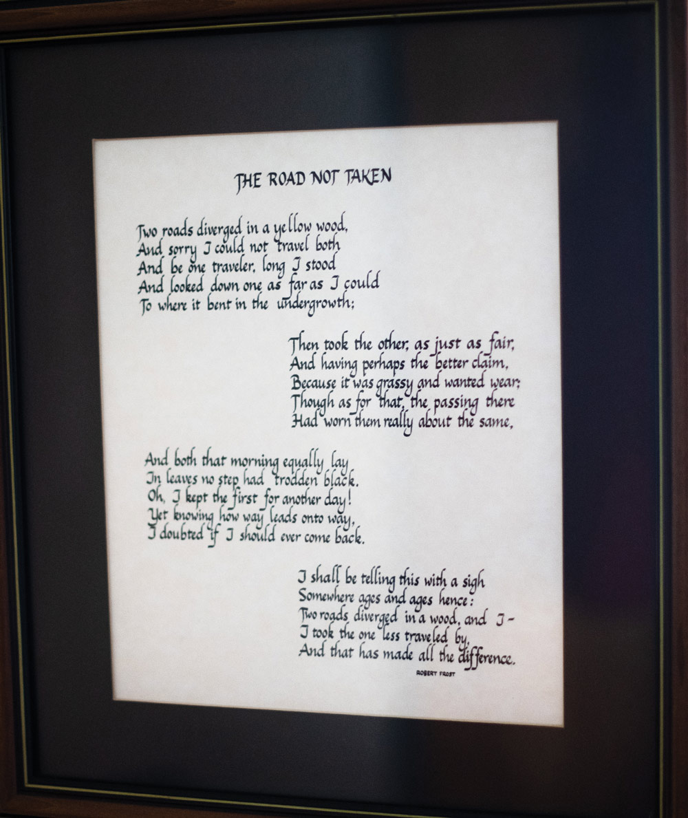 a framed handwritten poster of the Robert Frost poem "The Road Not Taken"