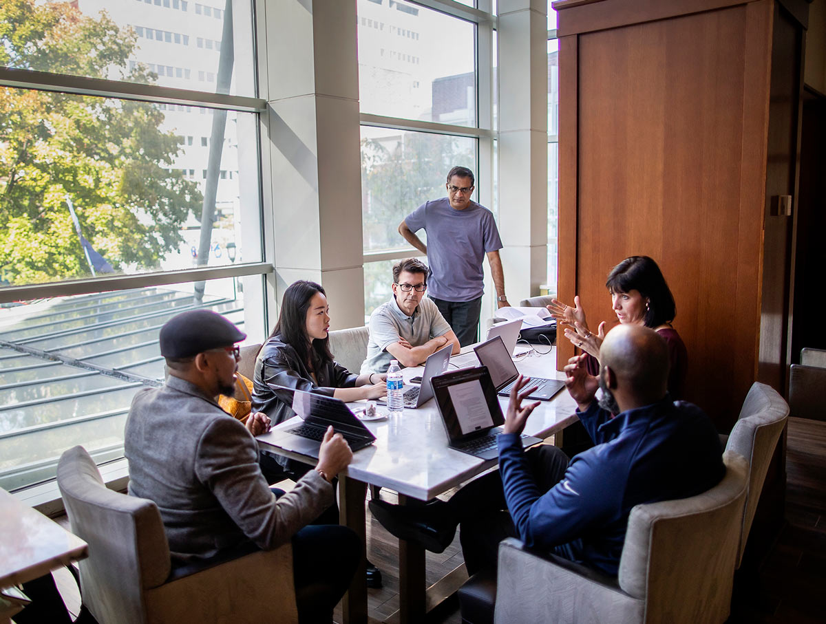 group of people sitting together at table with laptops open having a meeting