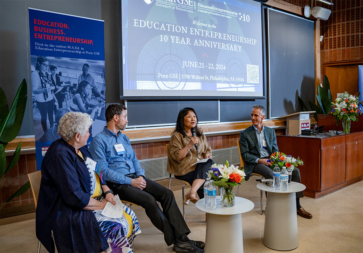 4 panelists in front of projector sitting and speaking with microphone