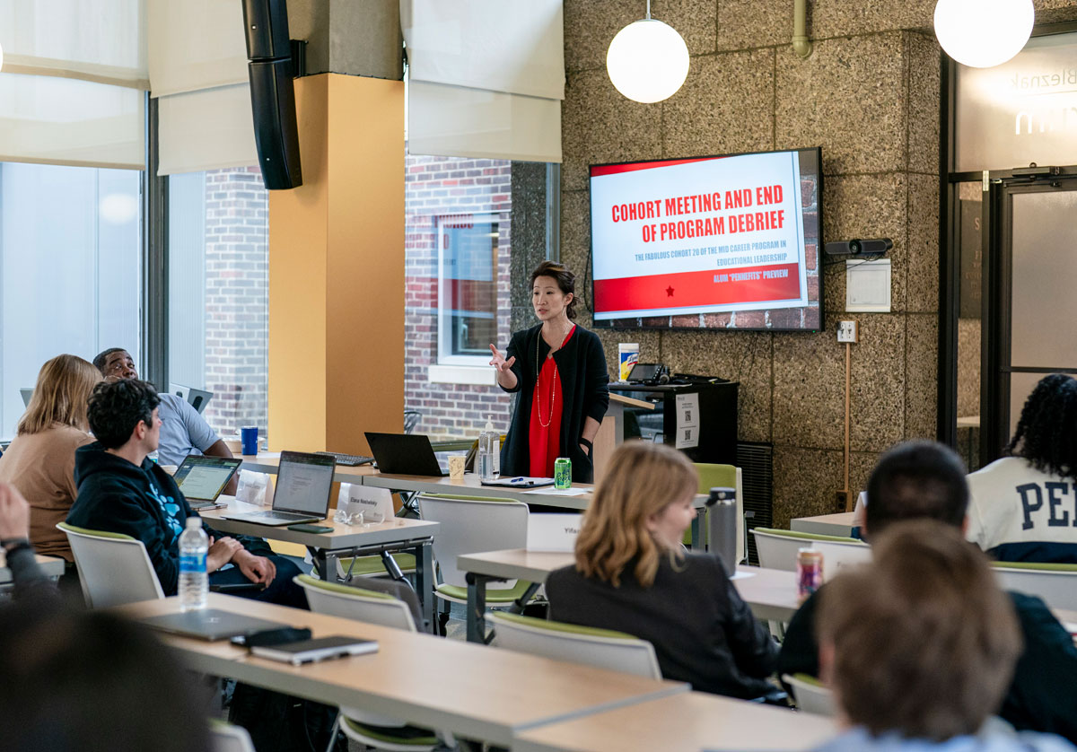 female speaker in front of seated class with powerpoint behind her