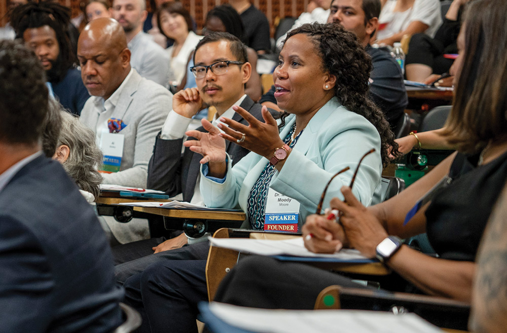 People engaged in a discussion in a lecture hall, with a woman speaking and others listening attentively.