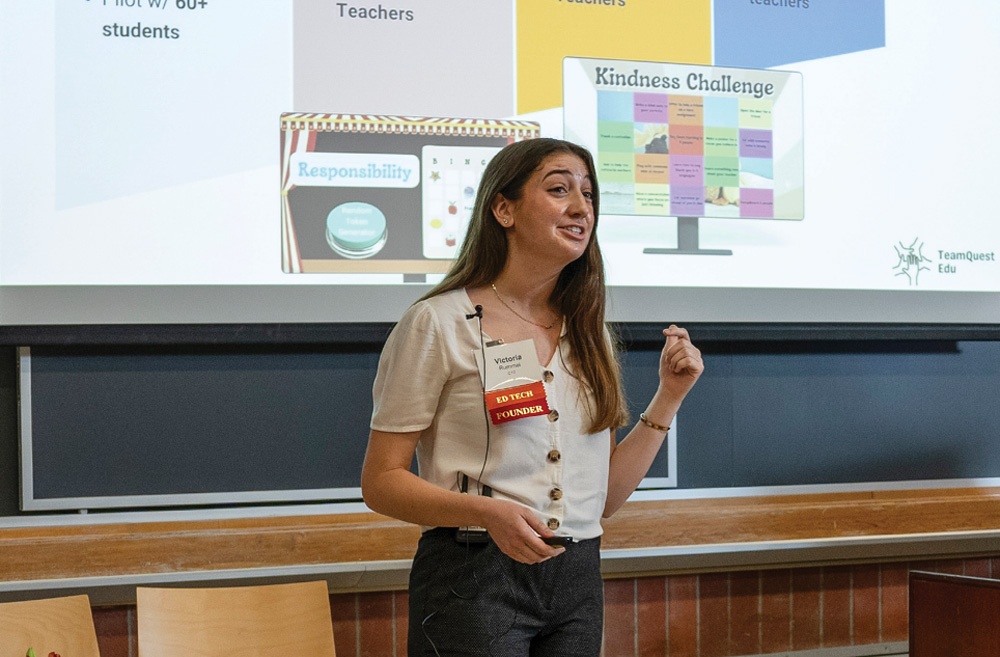 A woman presenting in a classroom with a slide displayed behind her.