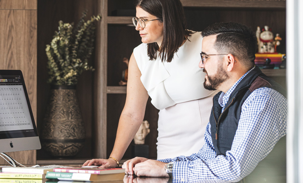 Two people working together at a desk in an office, focused on a computer screen.