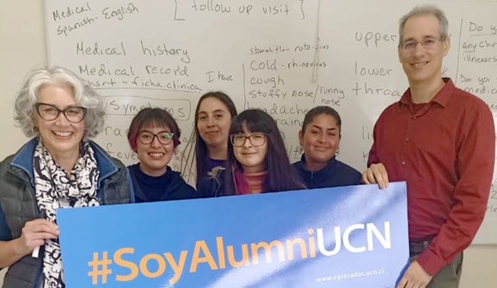 a woman and a man take a group photo with four young women while holding a sign that reads “#SoyAlumniUCN”